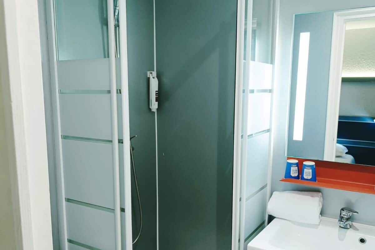 A shower with a glass door, a white sink, and a mirror above it.