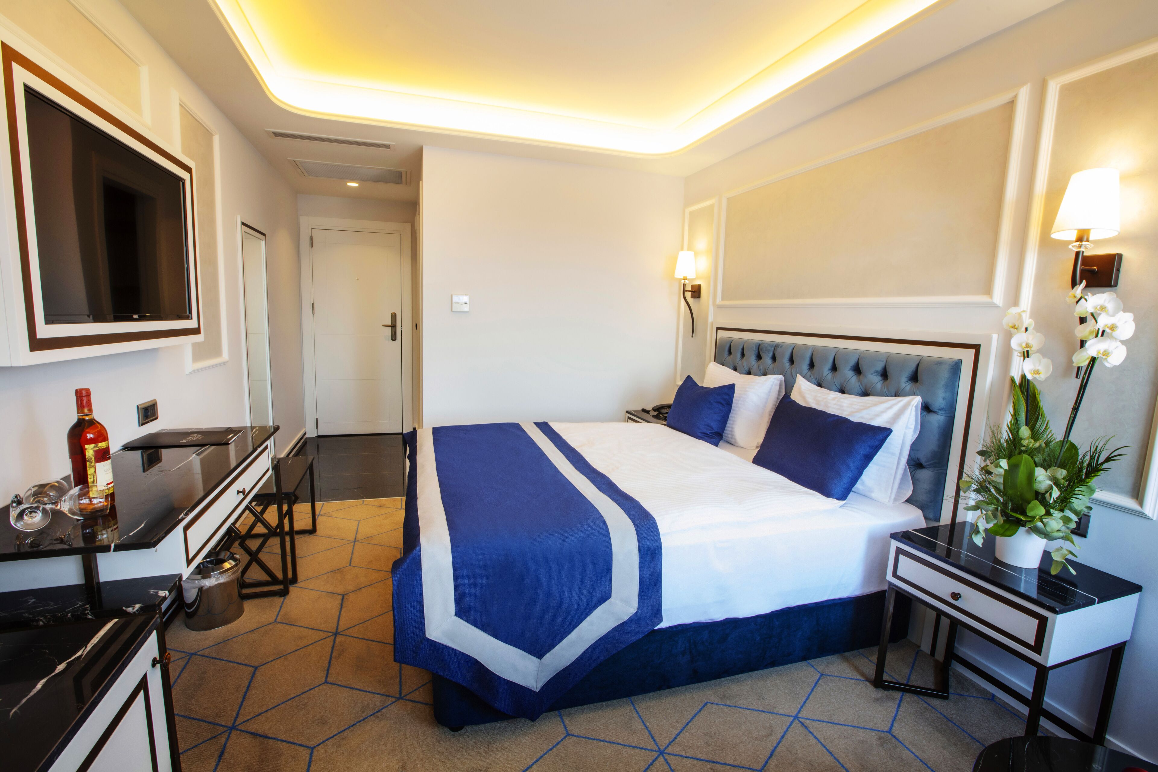Habitación de hotel con cama, mesita de noche, lámpara y televisión en la pared.
