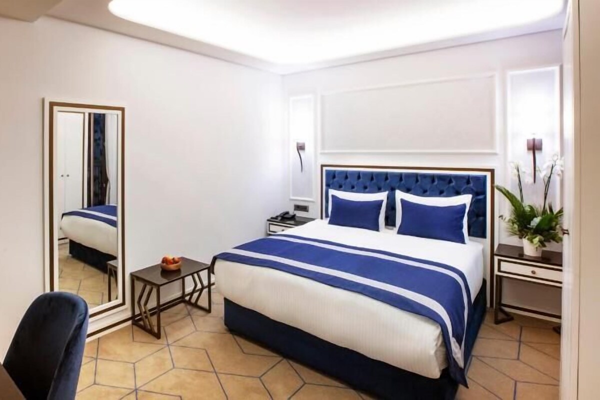 Une chambre d’hôtel avec un grand lit, une table de chevet, un miroir et un bureau avec une chaise.