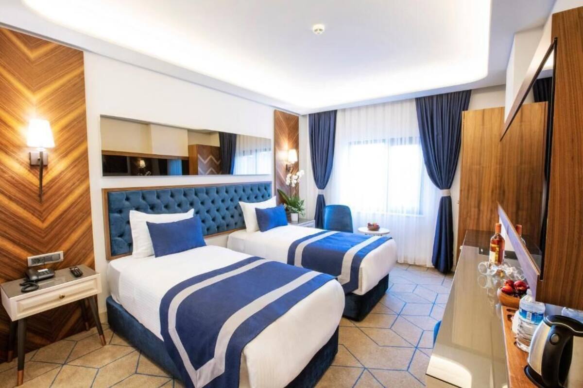 Habitació d'hotel amb dos llits, un mirall gran, escriptori amb làmpada i un minibar.