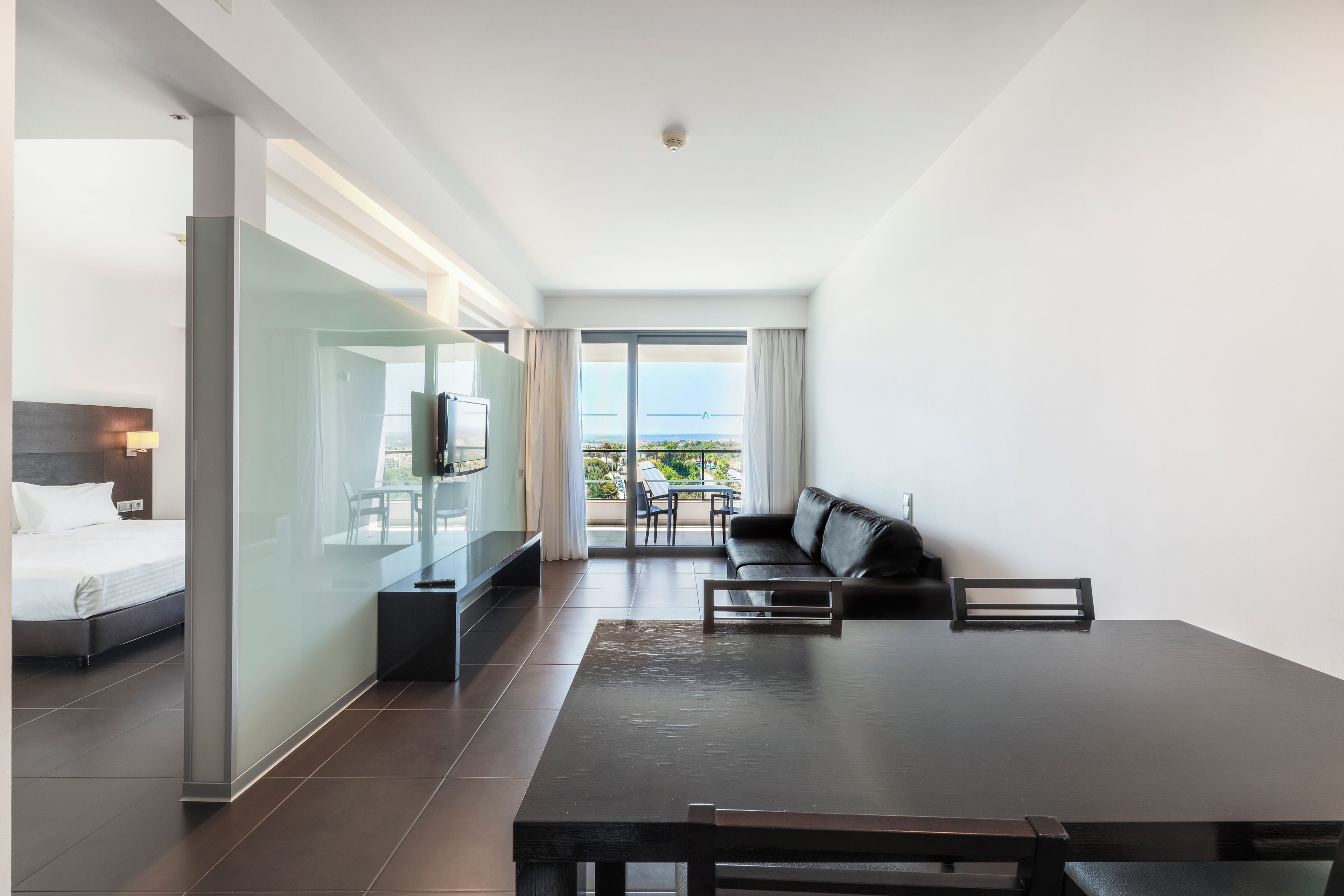 Ein Hotelzimmer mit Bett, Fernseher, Sofa und einem Balkon mit Blick.