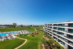 Un hotel moderno con piscina en la azotea, extensas áreas verdes y un cielo azul despejado.