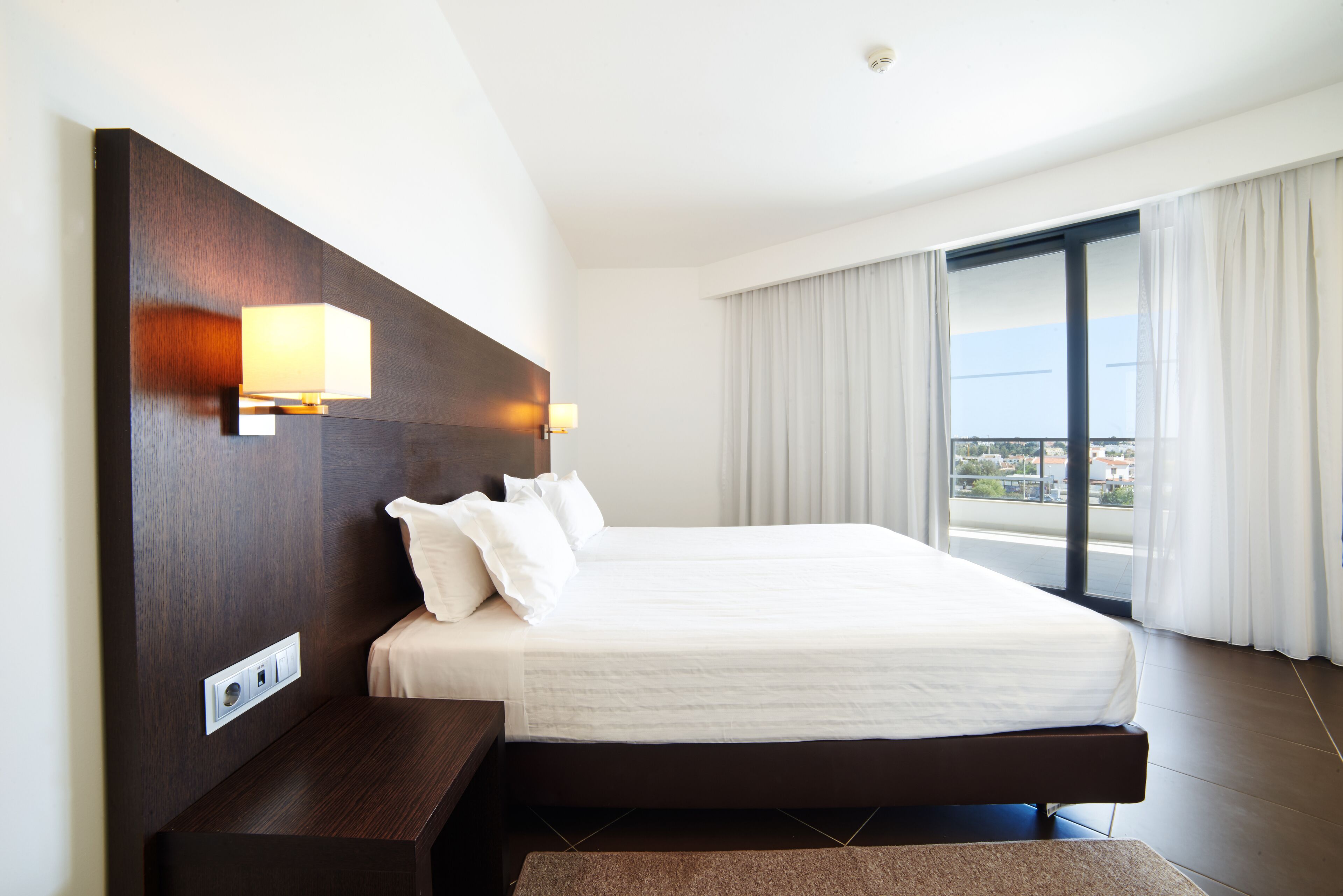 A large bed with a dark headboard, a bedside table, and a wall-mounted lamp.