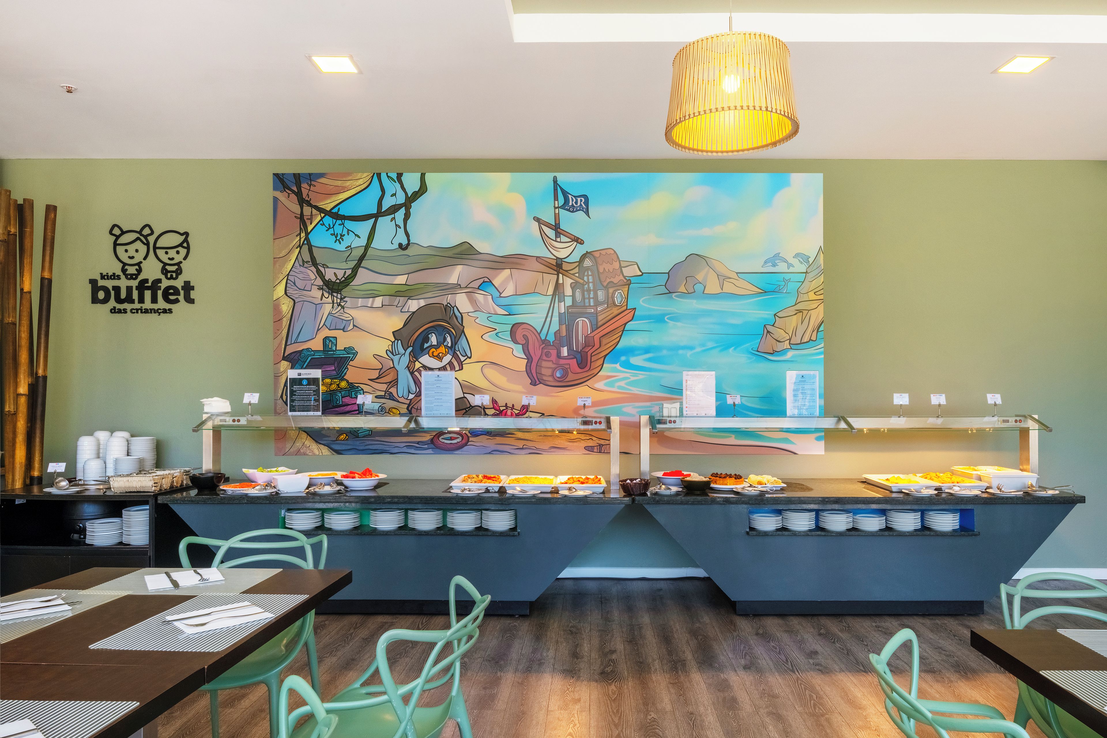A buffet area with a mural of a seascape and a penguin, buffet counters with various dishes, and green chairs.