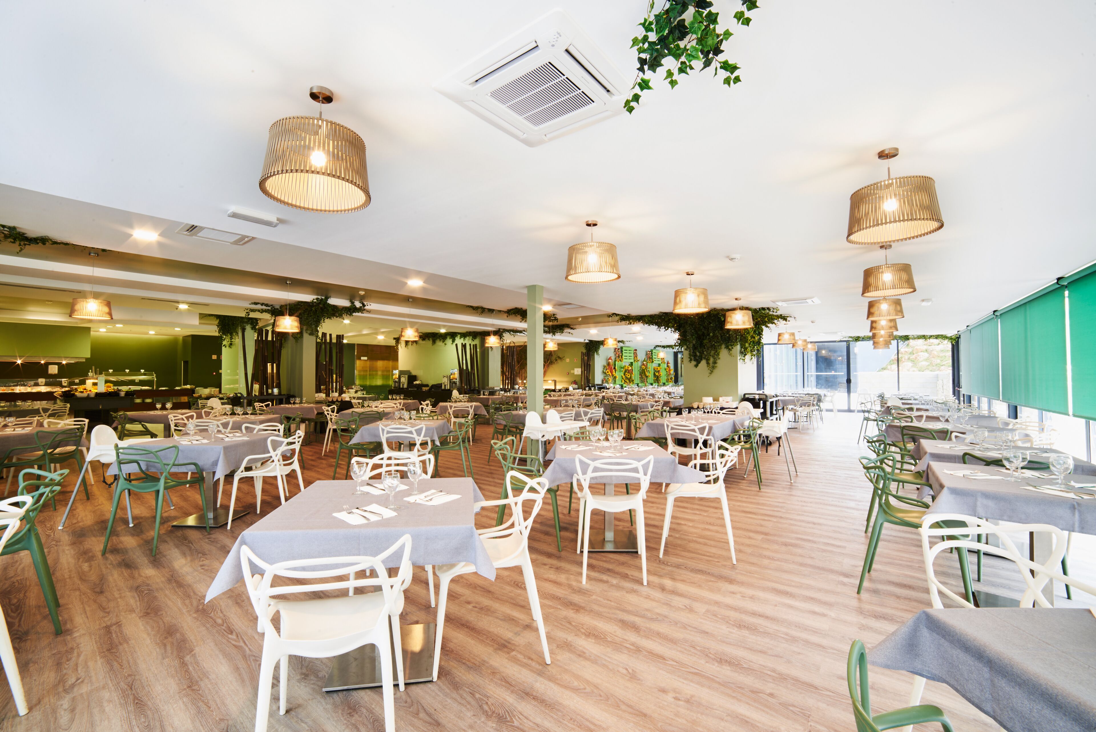 A spacious restaurant with multiple dining tables and chairs, a wooden floor, and hanging wicker lamps.