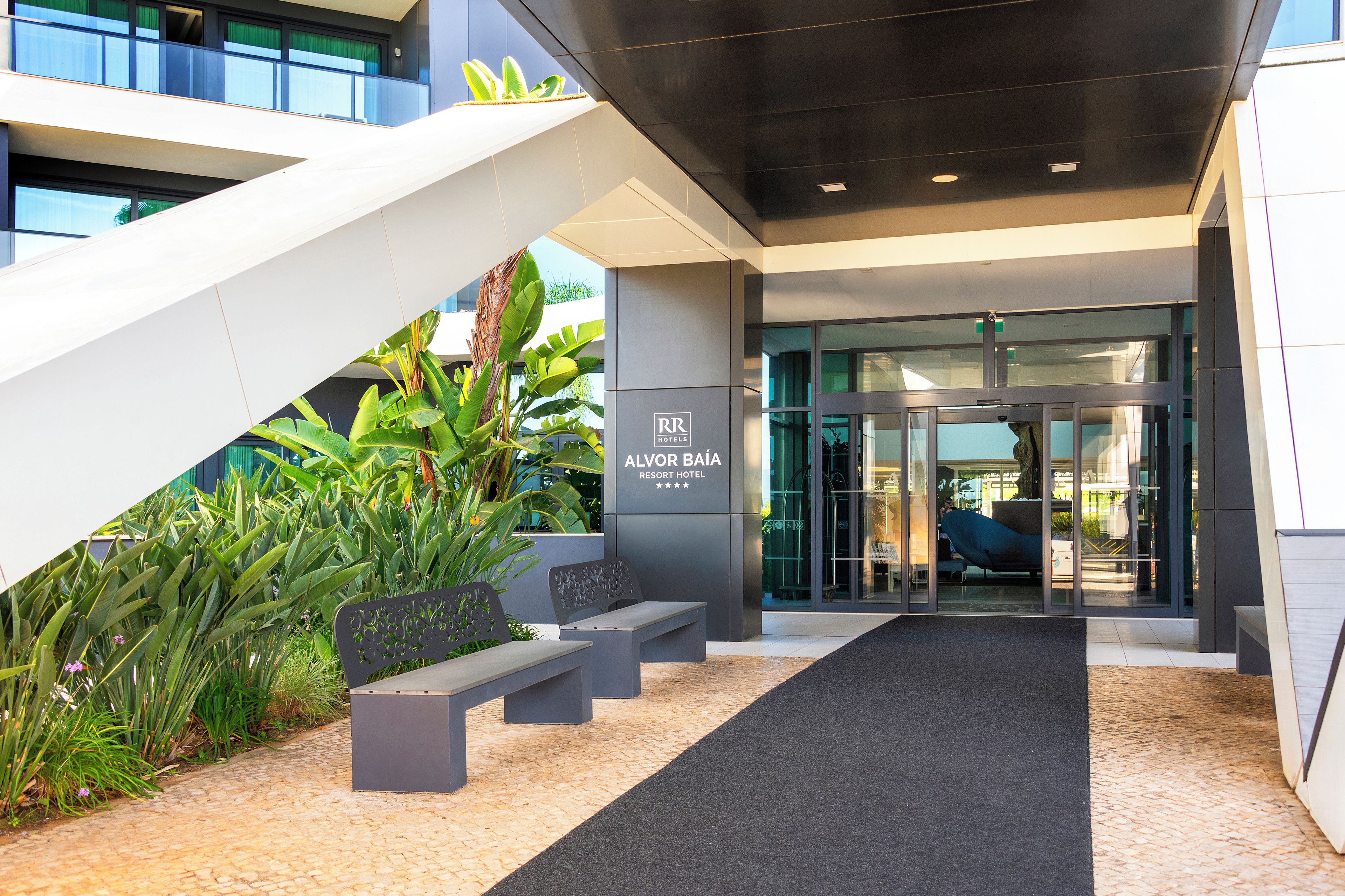 A modern hotel entrance with a glass door, a staircase, and outdoor seating.
