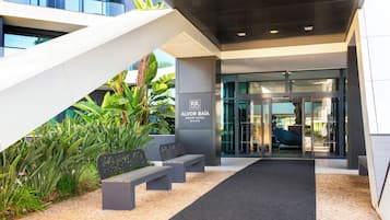 A modern hotel entrance with a glass door, a staircase, and outdoor seating.