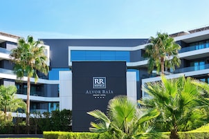 Un moderno edificio de hotel con un letrero llamativo para 'Alvor Baía Resort Hotel' y una vista despejada de la vegetación circundante.