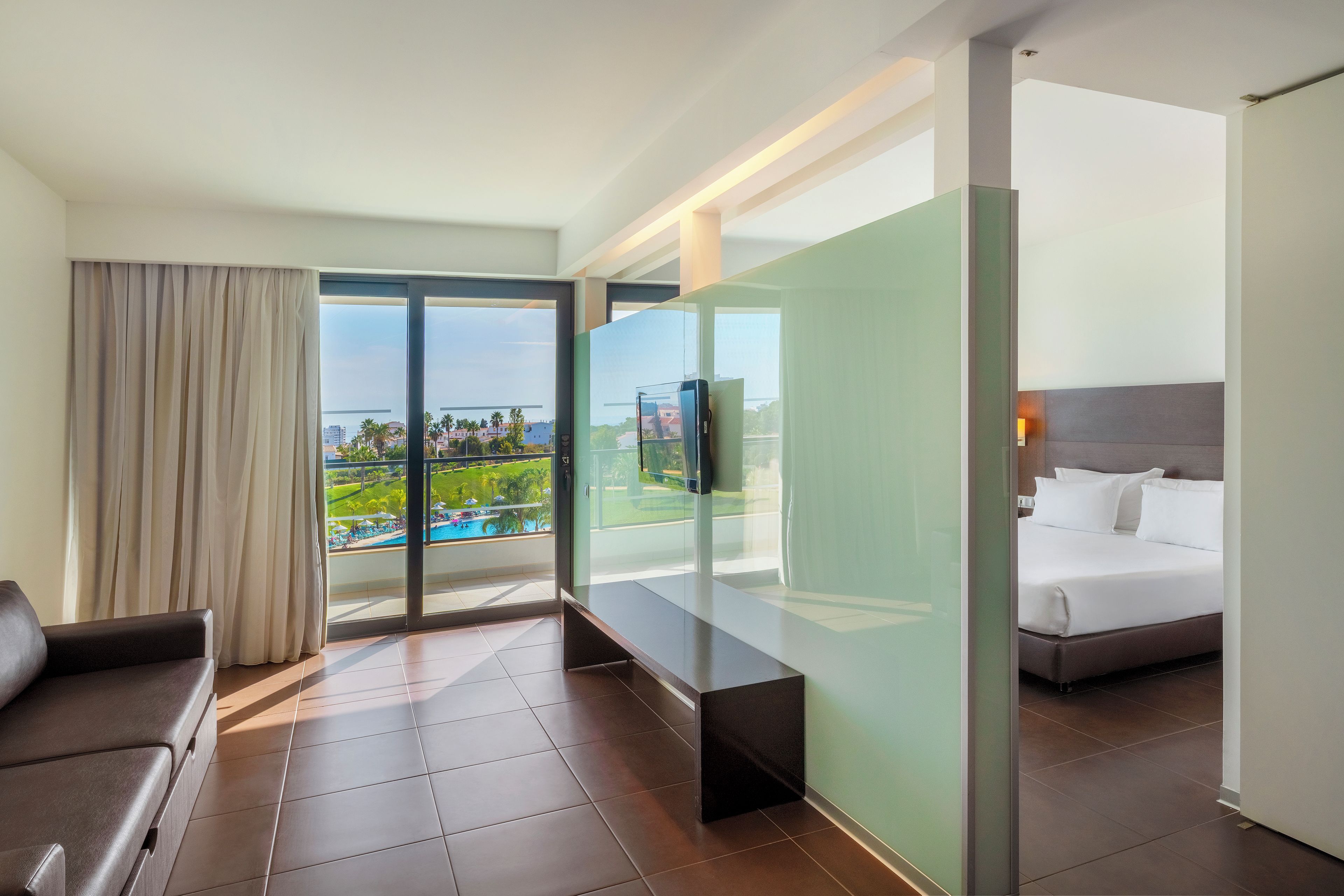 Habitación de hotel con cama, sofá, televisión y balcón con vista a la piscina.