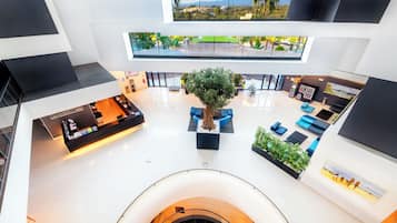 Un vestíbulo amplio con una zona de estar central, un mostrador de recepción y una escalera que conduce a un nivel superior.