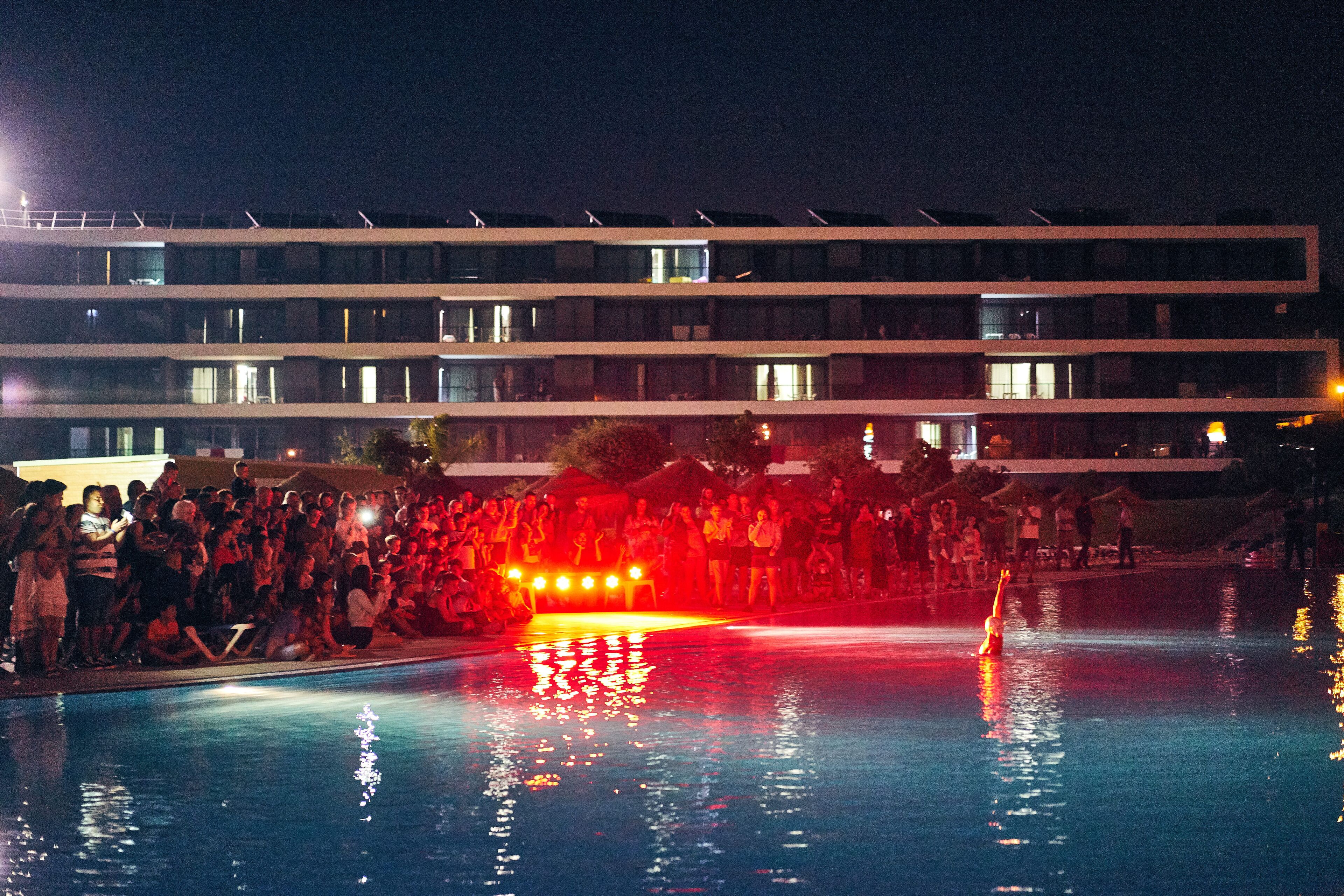 Una piscina con gente y un edificio al fondo.