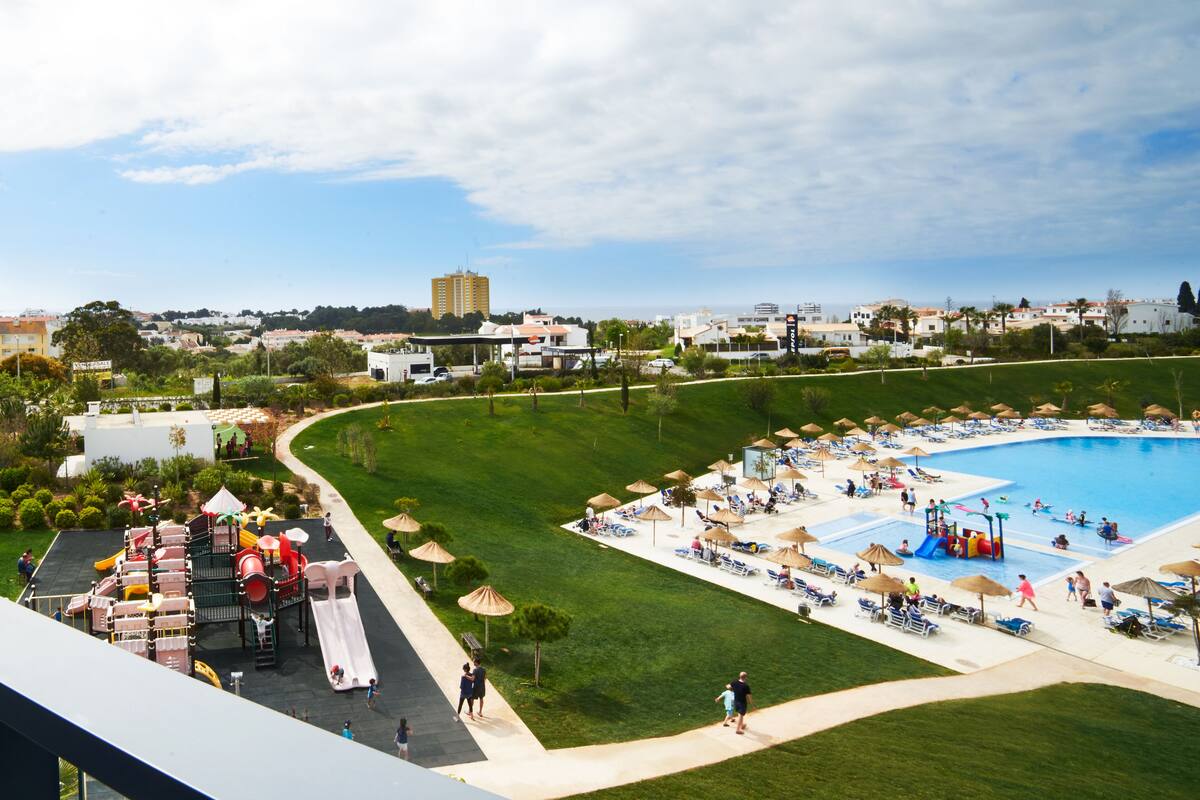 Een resort met een groot zwembad, een speeltuin en een gazon met ligbedden.