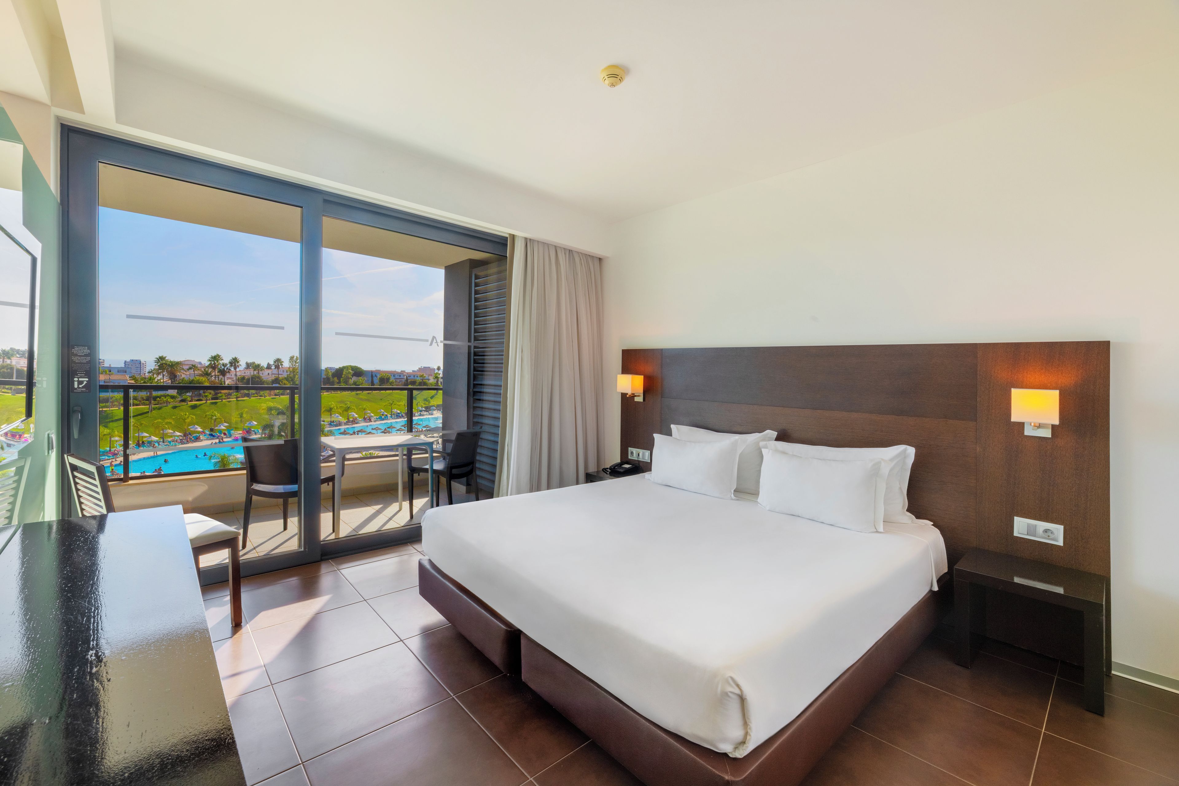 Habitación de hotel con una cama grande, un escritorio, una silla, un teléfono y vistas a una piscina.