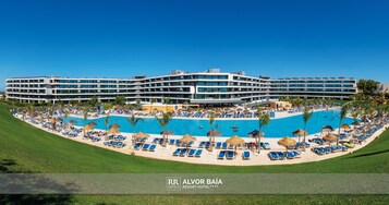 A resort hotel with a large pool, sun loungers, and a well-maintained lawn.