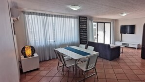 Un comedor con una mesa y sillas, un sofá, un televisor y una pared con una lista de destinos.