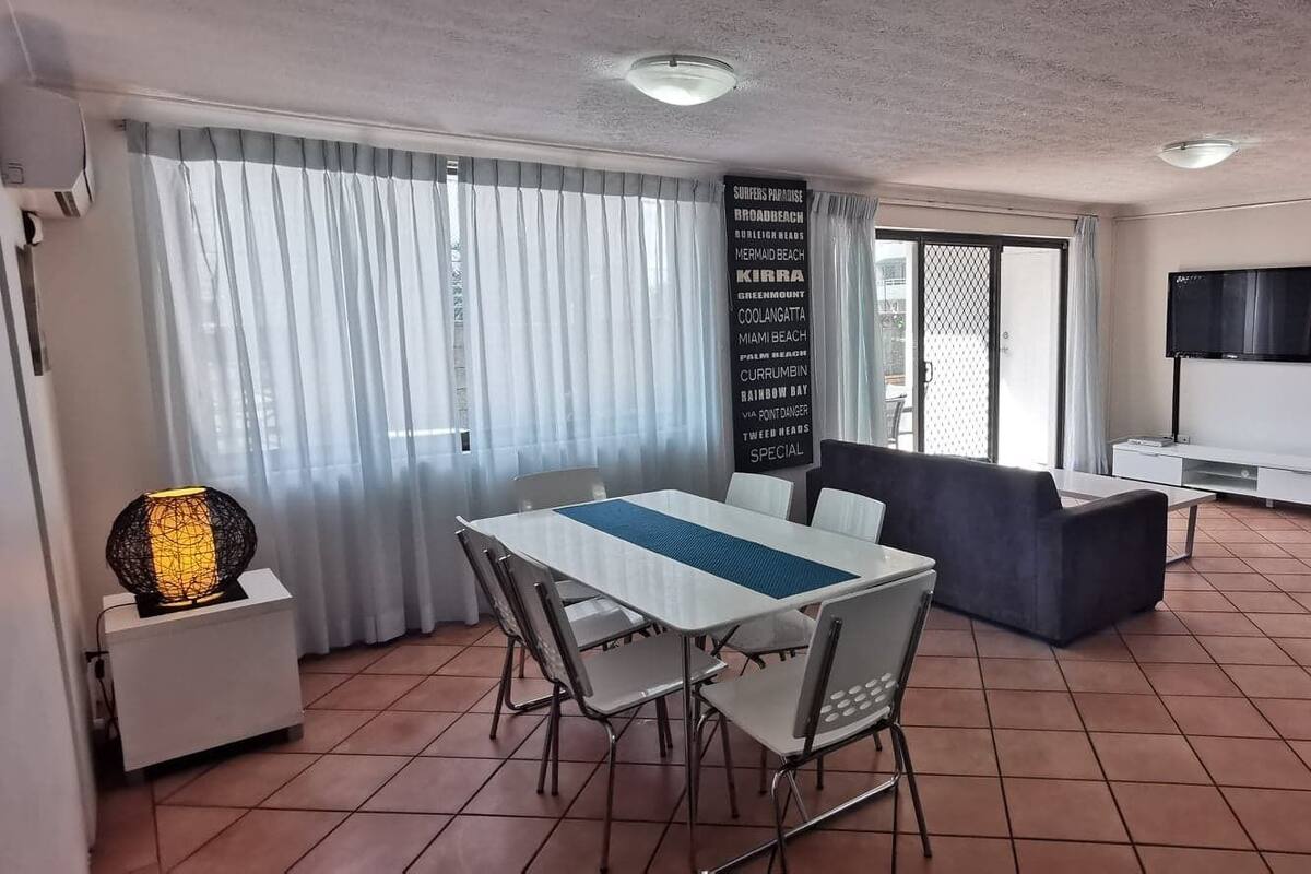 Un comedor con una mesa y sillas, un sofá, un televisor y una pared con una lista de destinos.