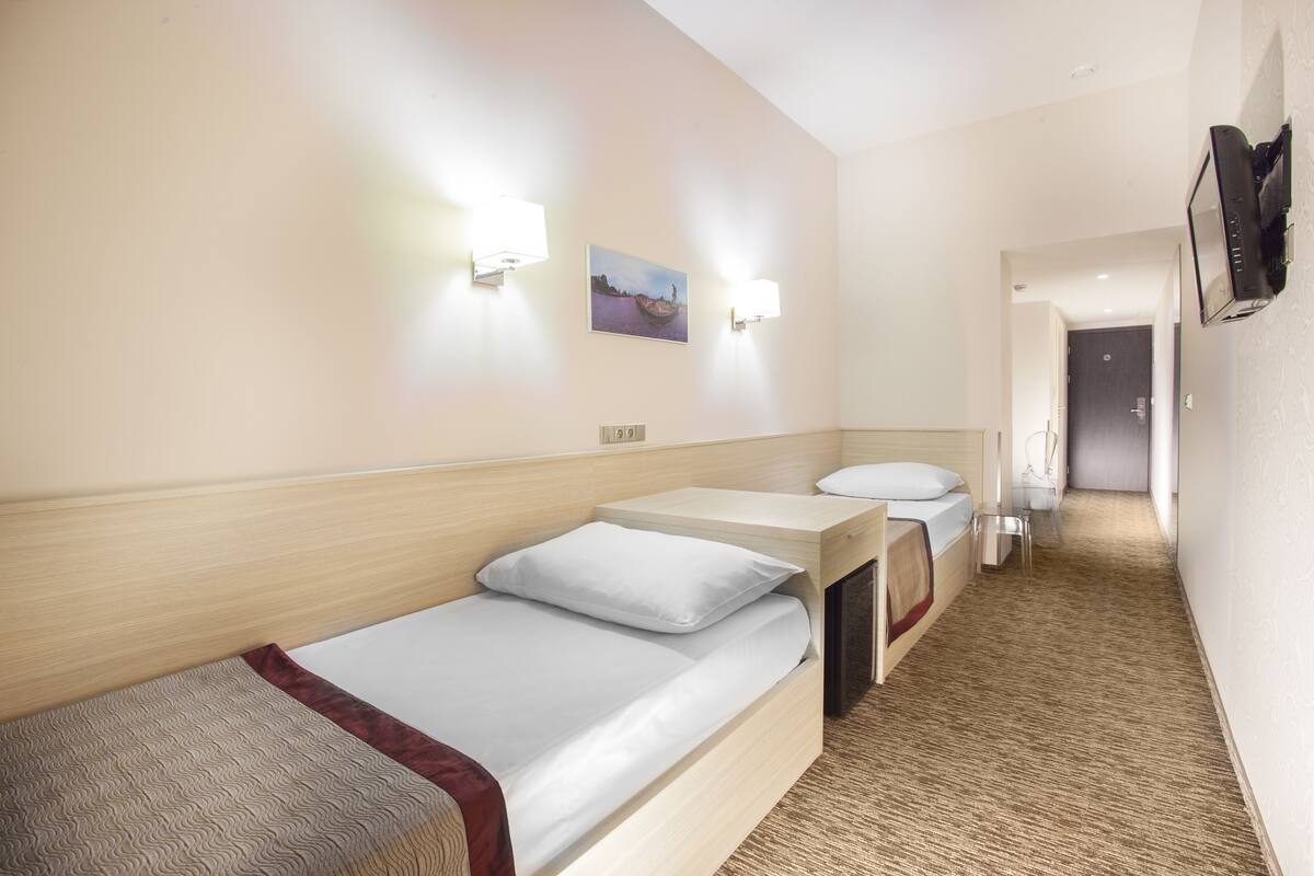 A hotel room with two single beds, a small table, a chair, and a television mounted on the wall.
