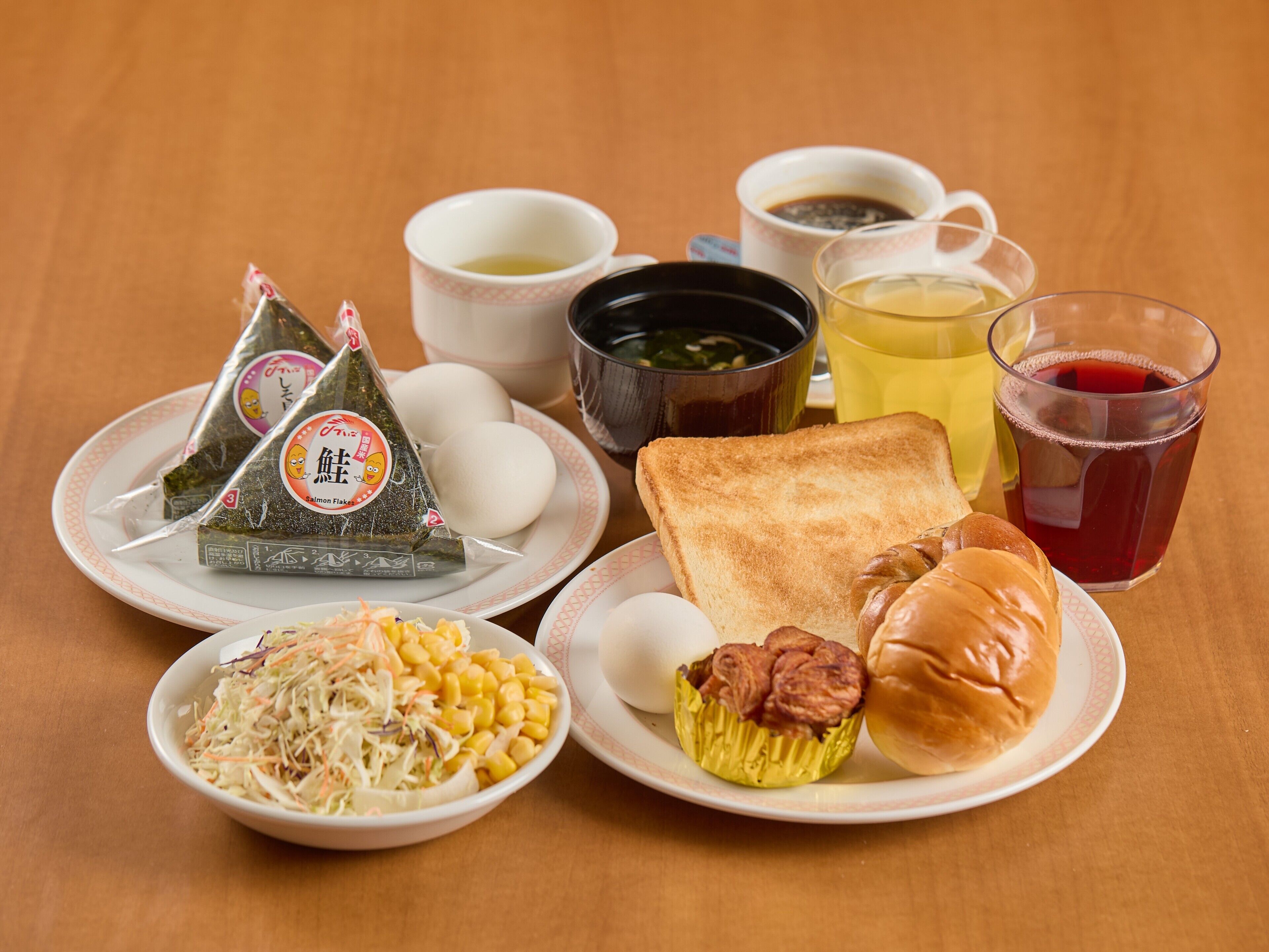 Una mesa con diferentes alimentos, como bolas de arroz, tostadas, un panecillo, ensalada y una taza de té.