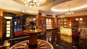 A lobby with a marble floor, a central round table with a floral arrangement, a reception desk, and a Coca-Cola refrigerator. - Hotel Blion Naha (Naha)