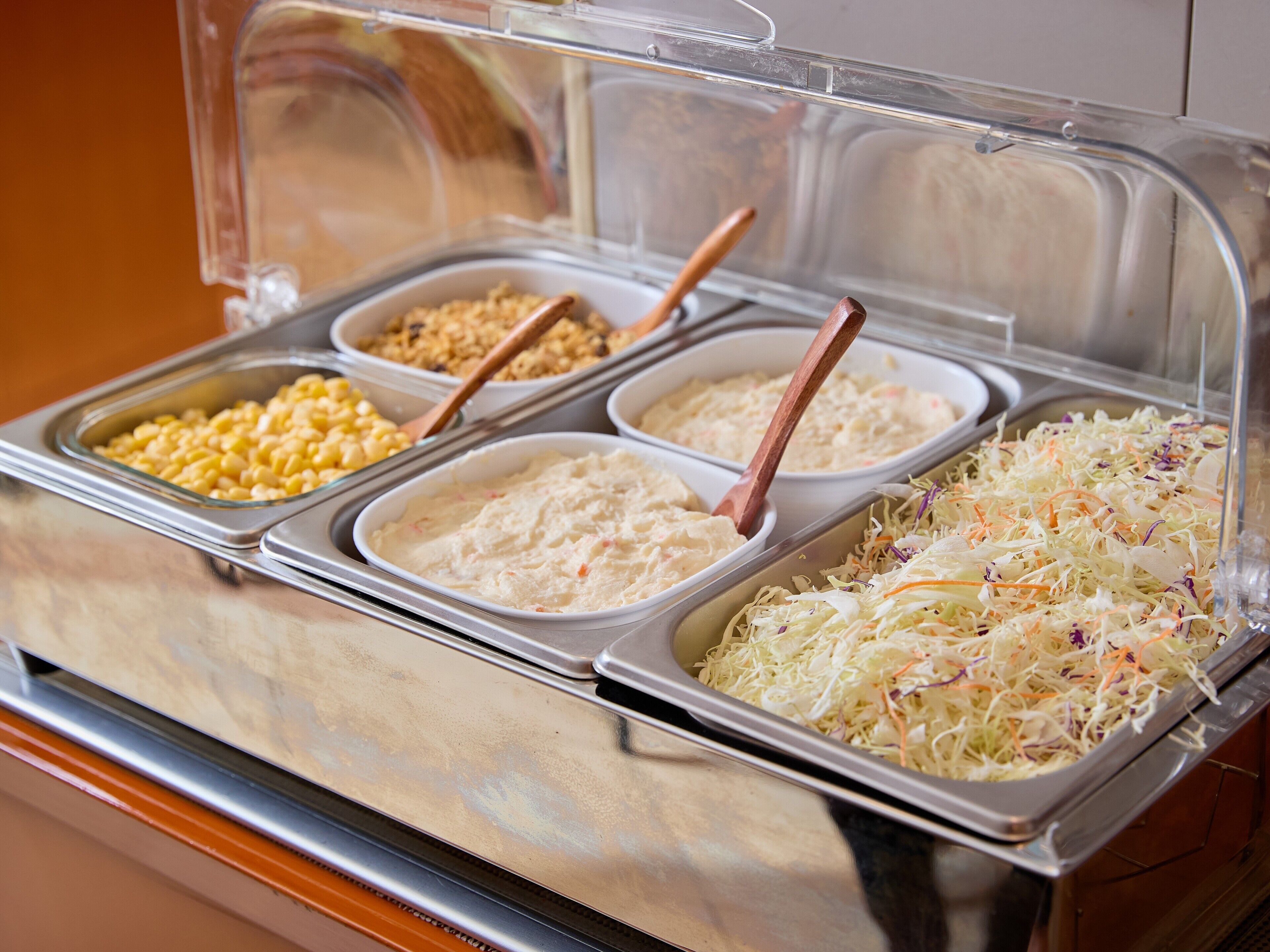 A buffet with various food options including corn, a creamy dish, and coleslaw.