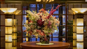 A round table with a floral arrangement in a lobby with glass doors and two lamps. - Hotel Blion Naha (Naha)