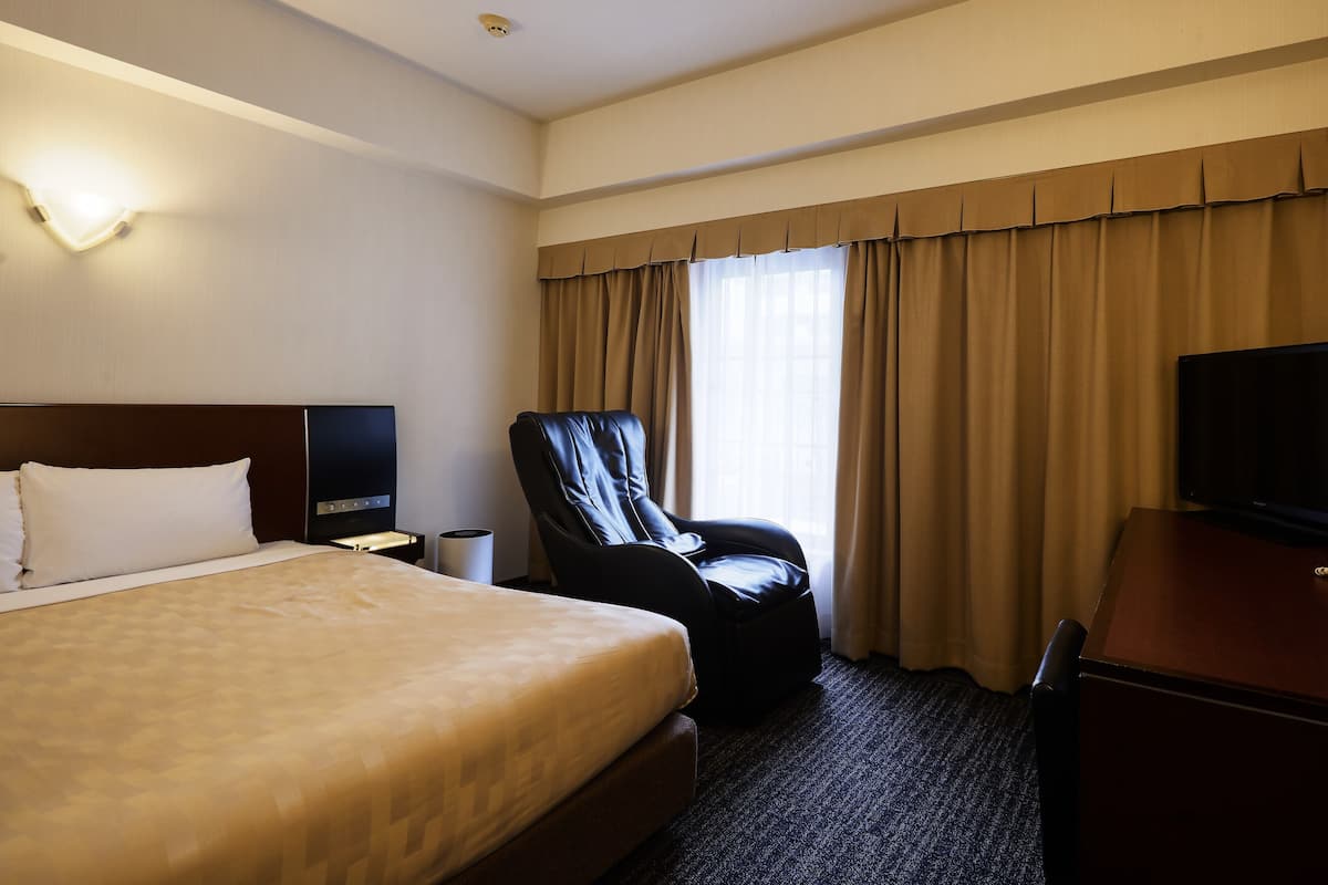 A hotel room with a bed, a desk, a chair, a TV, and a window with curtains.