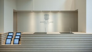 A modern reception area with a tiled wall displaying the logo and name 'Agora Place Abakusa'. There are two reception desks, one with a laptop and the other with a tablet. - Agora Place Tokyo Asakusa (Tokyo)