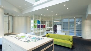 A modern hotel room with a large desk, a green sofa, and a glass-enclosed closet with neatly folded clothes. - Agora Place Tokyo Asakusa (Tokyo)