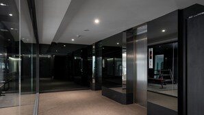 A modern interior with glass walls, a carpeted floor, and a visible elevator. - Myhotel CMYK Ratchada (Bangkok)