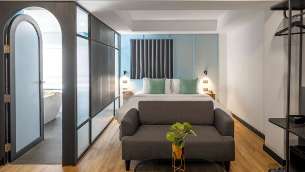 A modern bedroom with a large bed, a grey sofa, a small table with a plant, and a wardrobe. - Myhotel CMYK Ratchada (Bangkok)