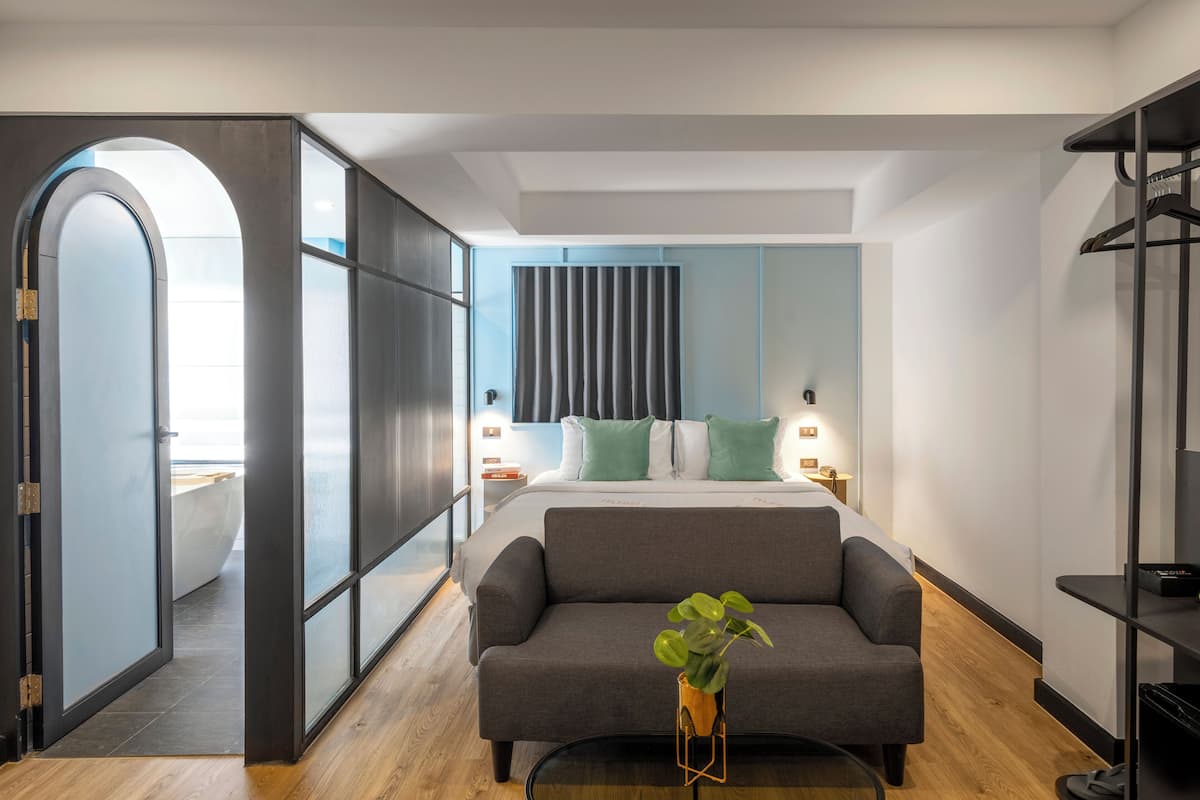 A modern bedroom with a large bed, a grey sofa, a small table with a plant, and a wardrobe.