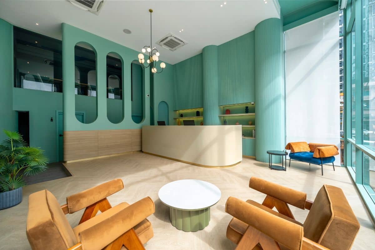 A modern lobby with teal walls, a reception desk, seating area, and large windows.