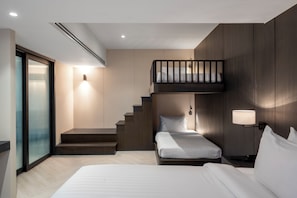 A modern hotel room with a bunk bed, a small desk, a nightstand, a lamp, and a staircase leading to an upper level.