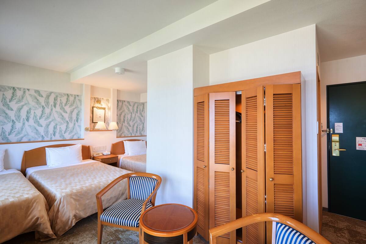Quarto de hotel com duas camas, uma mesa pequena, uma cadeira e um guarda-roupa.
