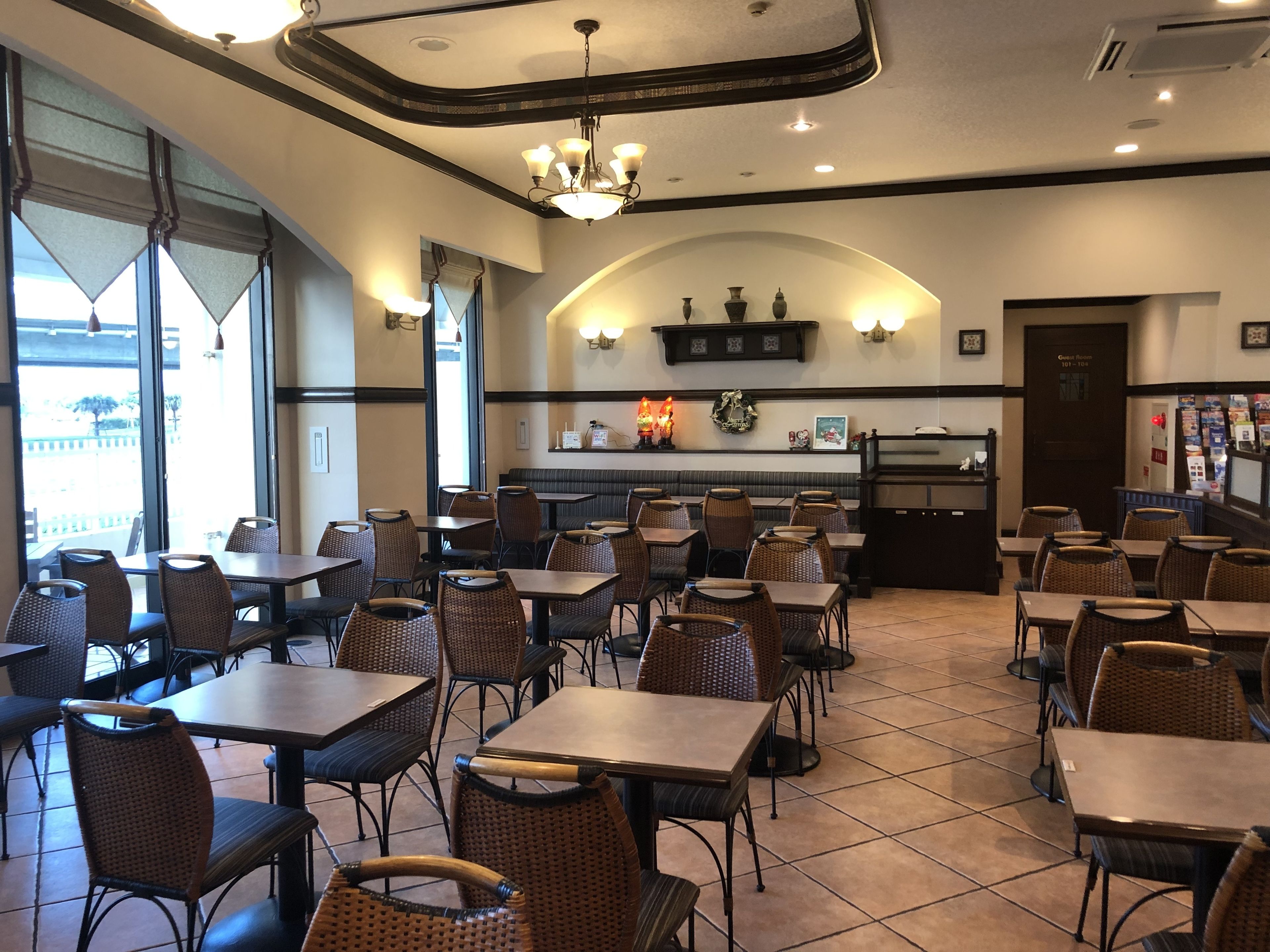 A restaurant interior with tables and wicker chairs, a chandelier, and a counter with a menu.