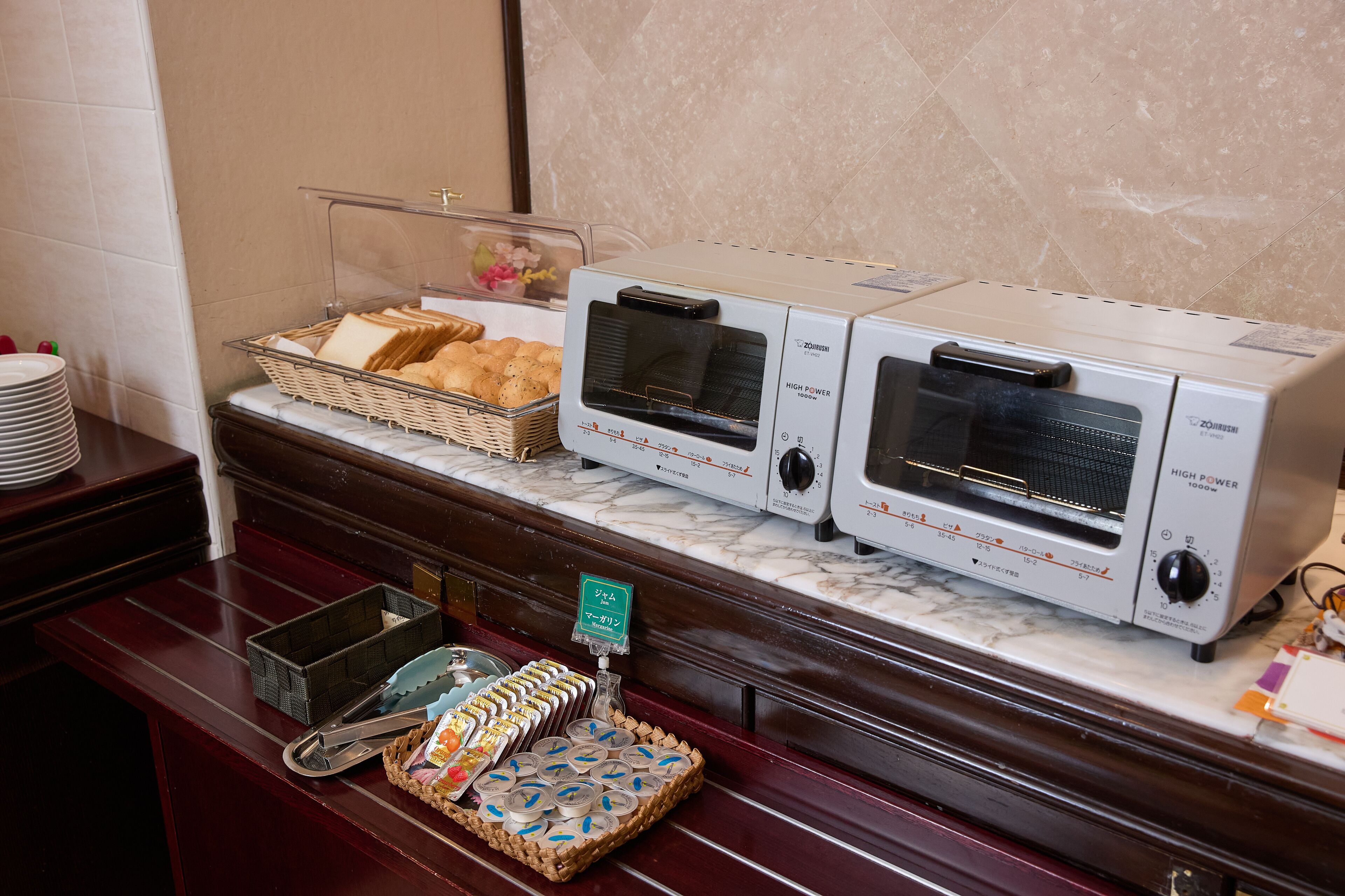 A buffet setup with two high-power toasters, a wicker basket with bread, and a tray with various pastries.