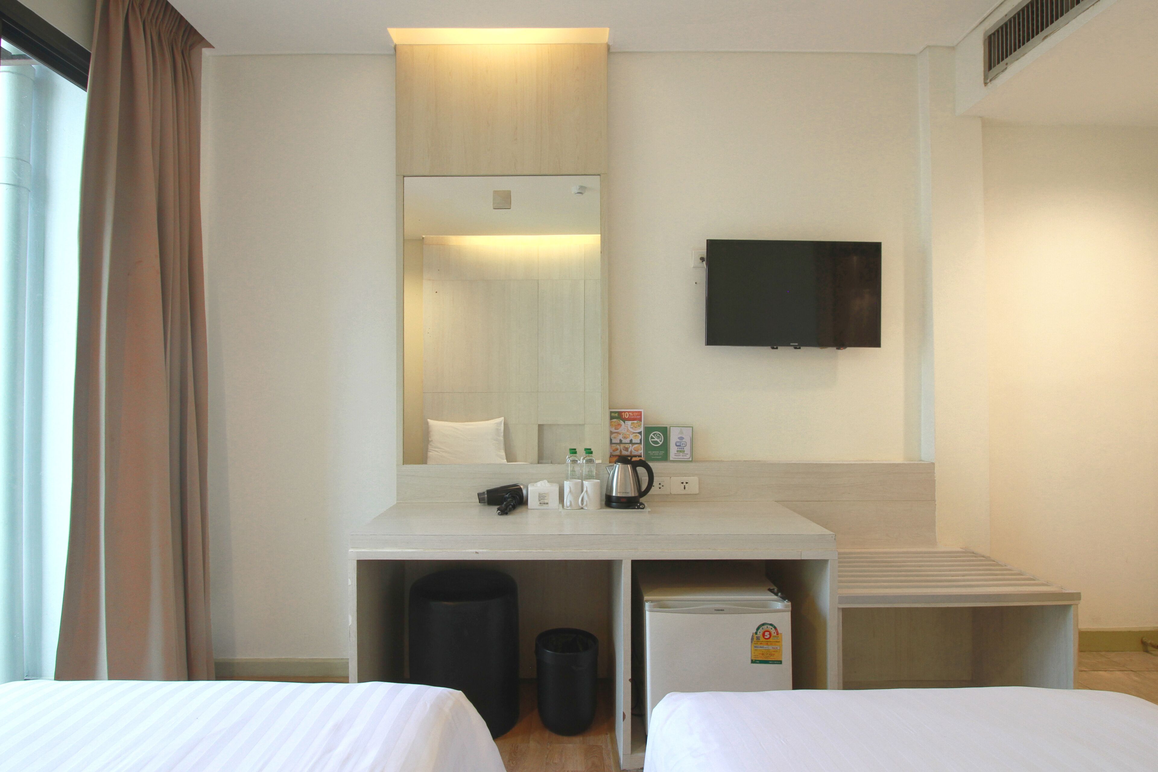 A hotel room with two beds, a desk with a mirror, a television, and a small refrigerator.