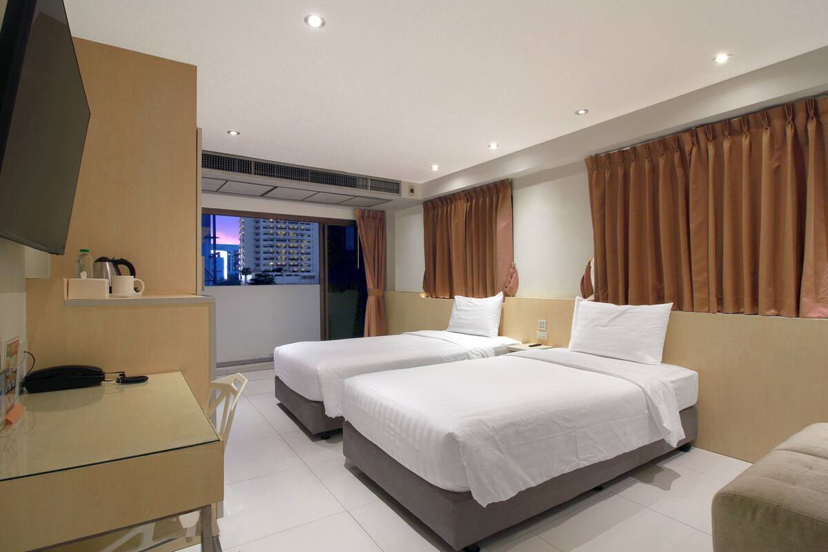 A hotel room with two beds, a desk with a telephone, and a view of the cityscape.