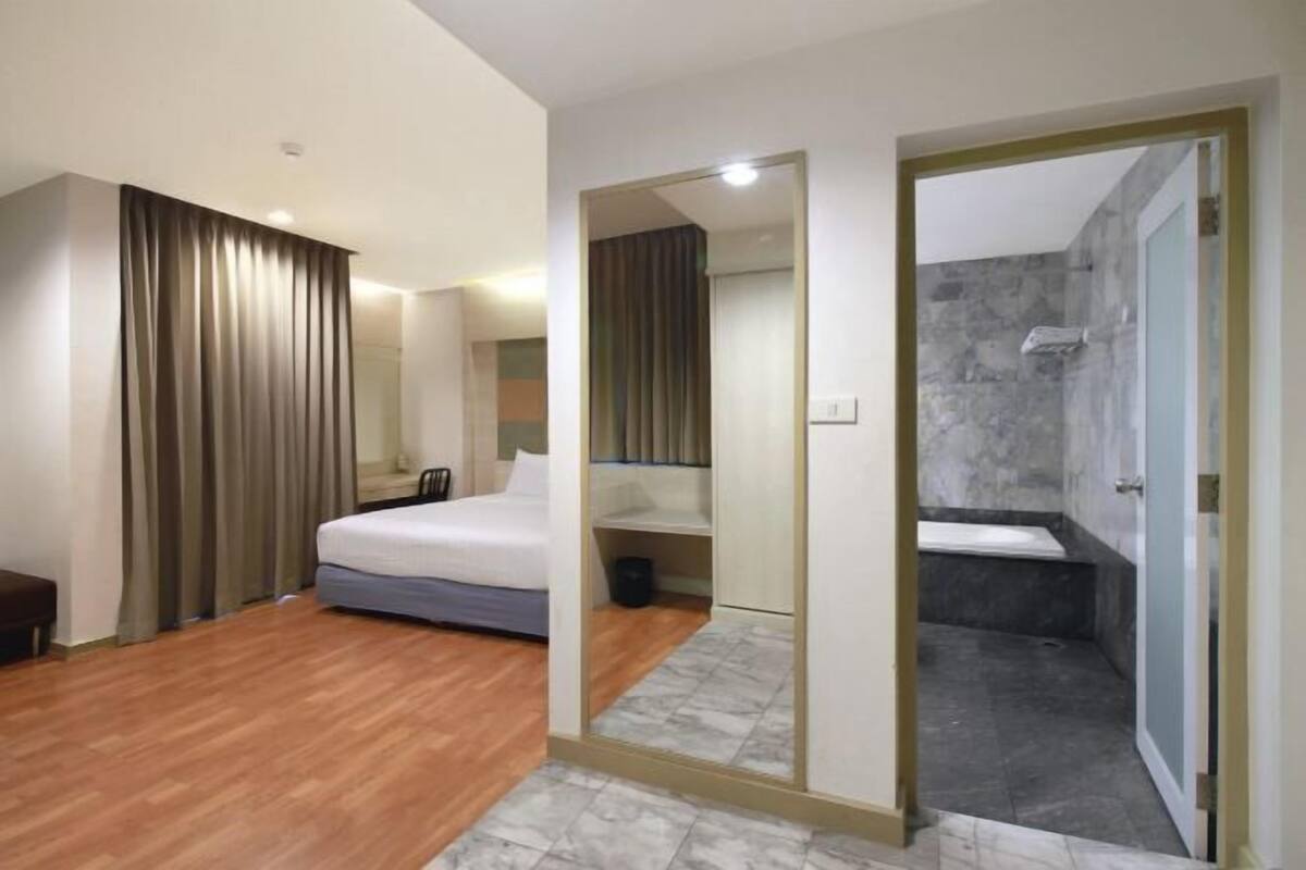 A hotel room with a bed, a mirror, a shower, and a wooden floor.