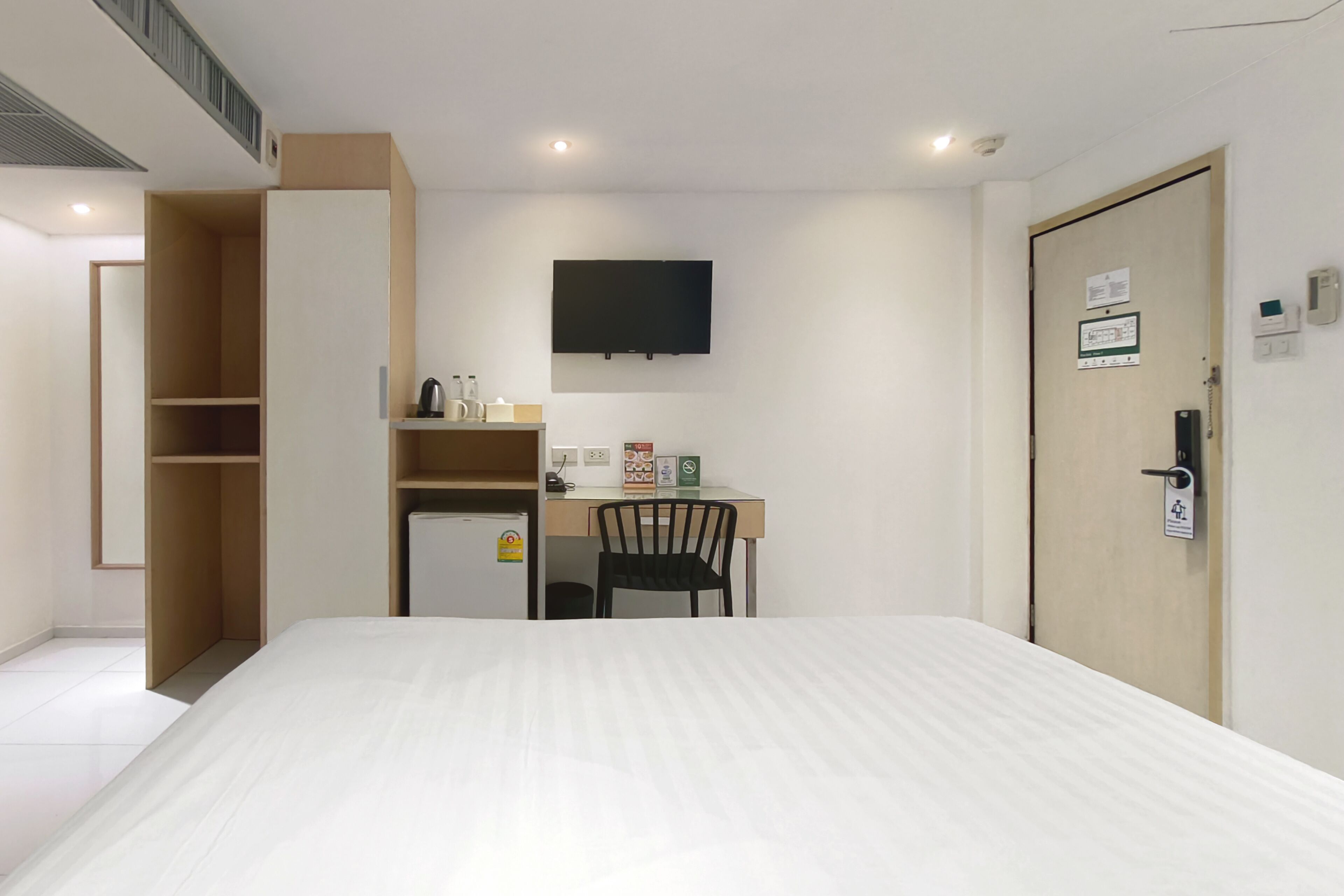 A hotel room with a bed, a desk with a chair, a television, and a door with a lock.