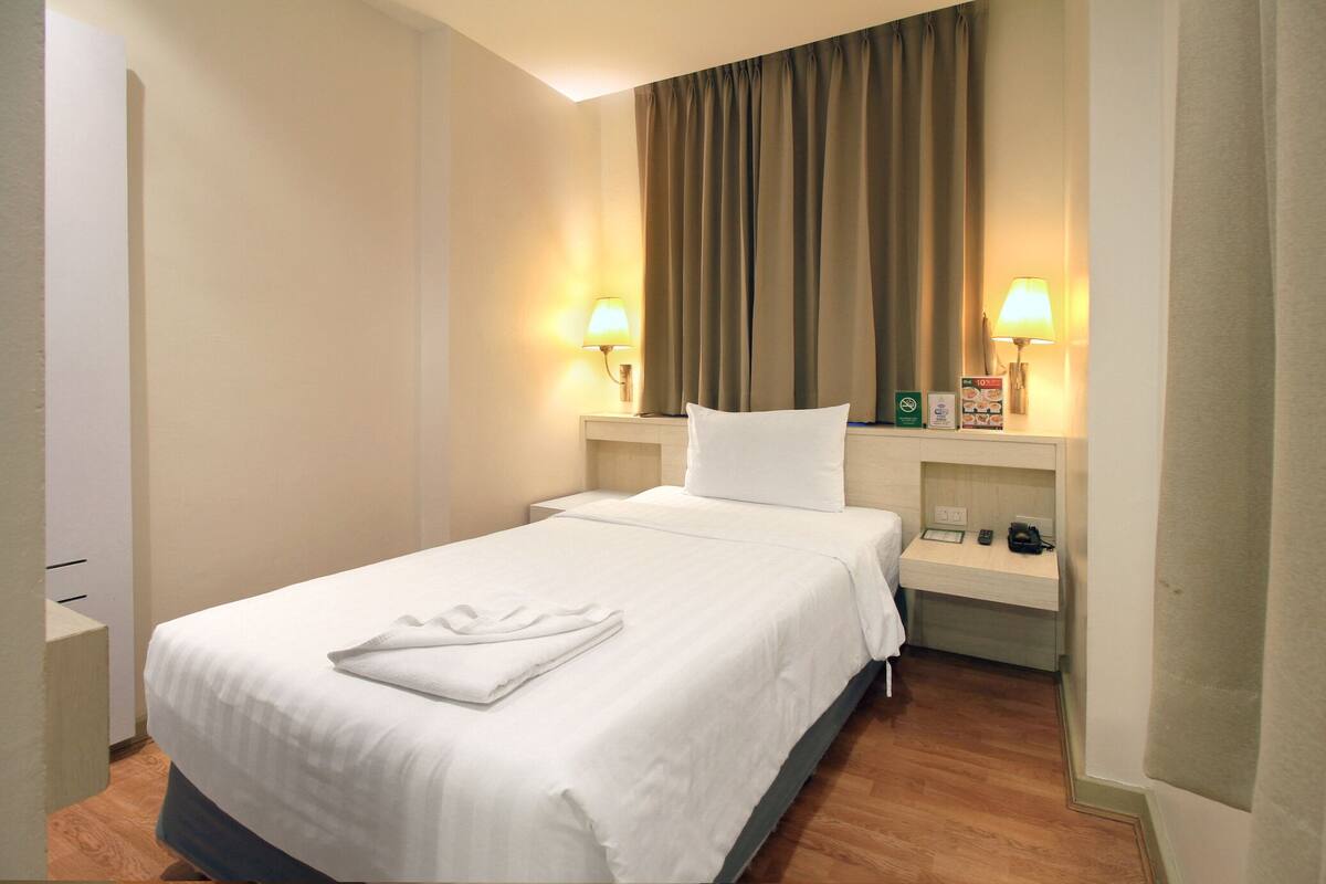 A hotel room with a bed, two bedside lamps, a nightstand, and a window with curtains.