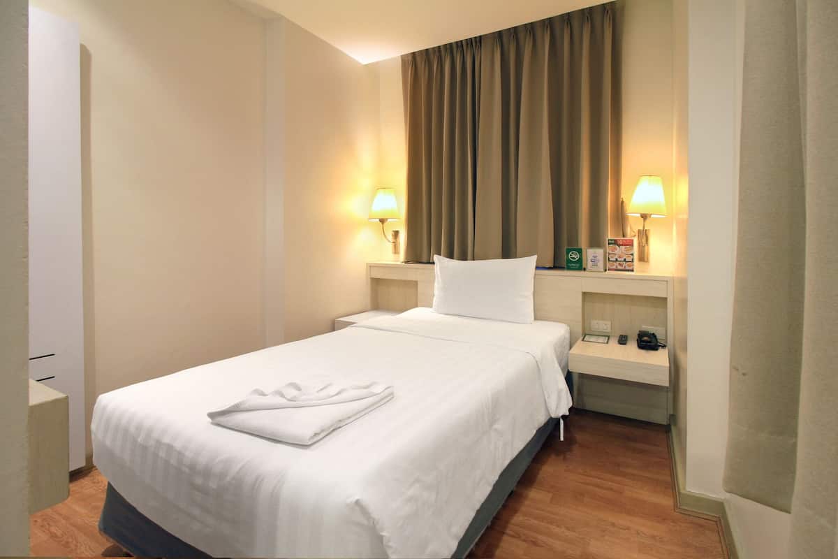 Quarto de hotel com cama, duas luminárias de cabeceira, mesa de cabeceira e janela com cortinas.