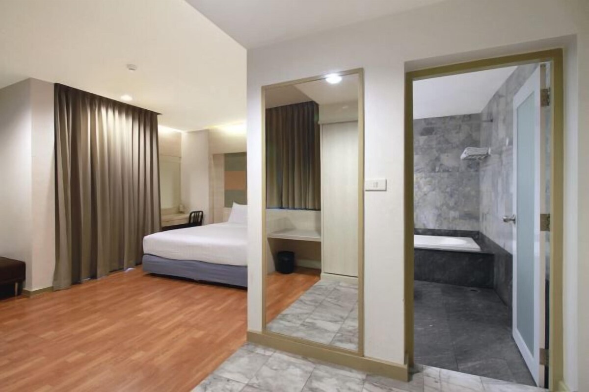 Een hotelkamer met een bed, een spiegel, een douche en een houten vloer.