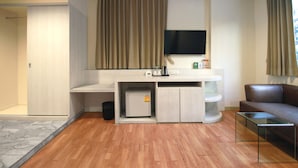 A modern hotel room with a wooden floor, a flat-screen TV mounted on the wall, a small refrigerator, a glass coffee table, and a leather sofa. - Ten Stars Hotel Pratunam (Bangkok)