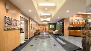 A hotel lobby with a reception desk, seating area, and a wall with a food menu. - Ten Stars Hotel Pratunam (Bangkok)