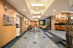 A hotel lobby with a reception desk, seating area, and a wall with a food menu. - Ten Stars Hotel Pratunam (Bangkok)