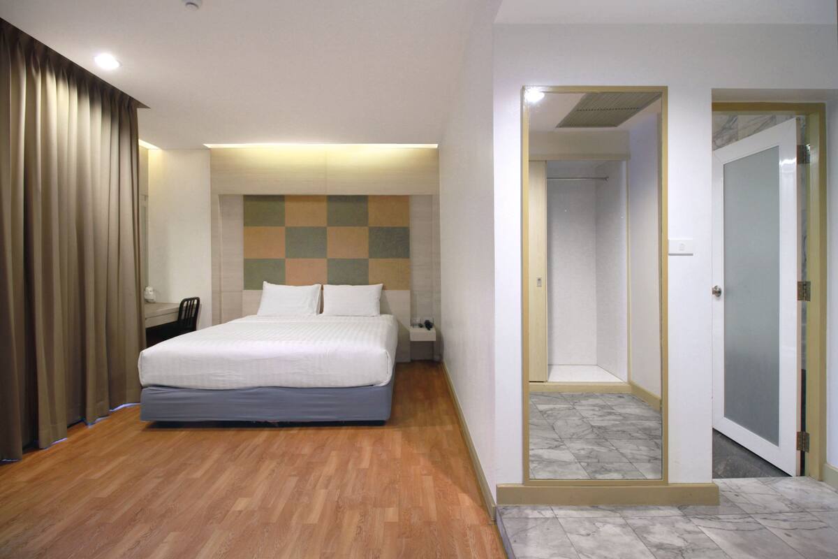 A hotel room with a bed, a nightstand, a chair, a checkered wall, and a door leading to another room.