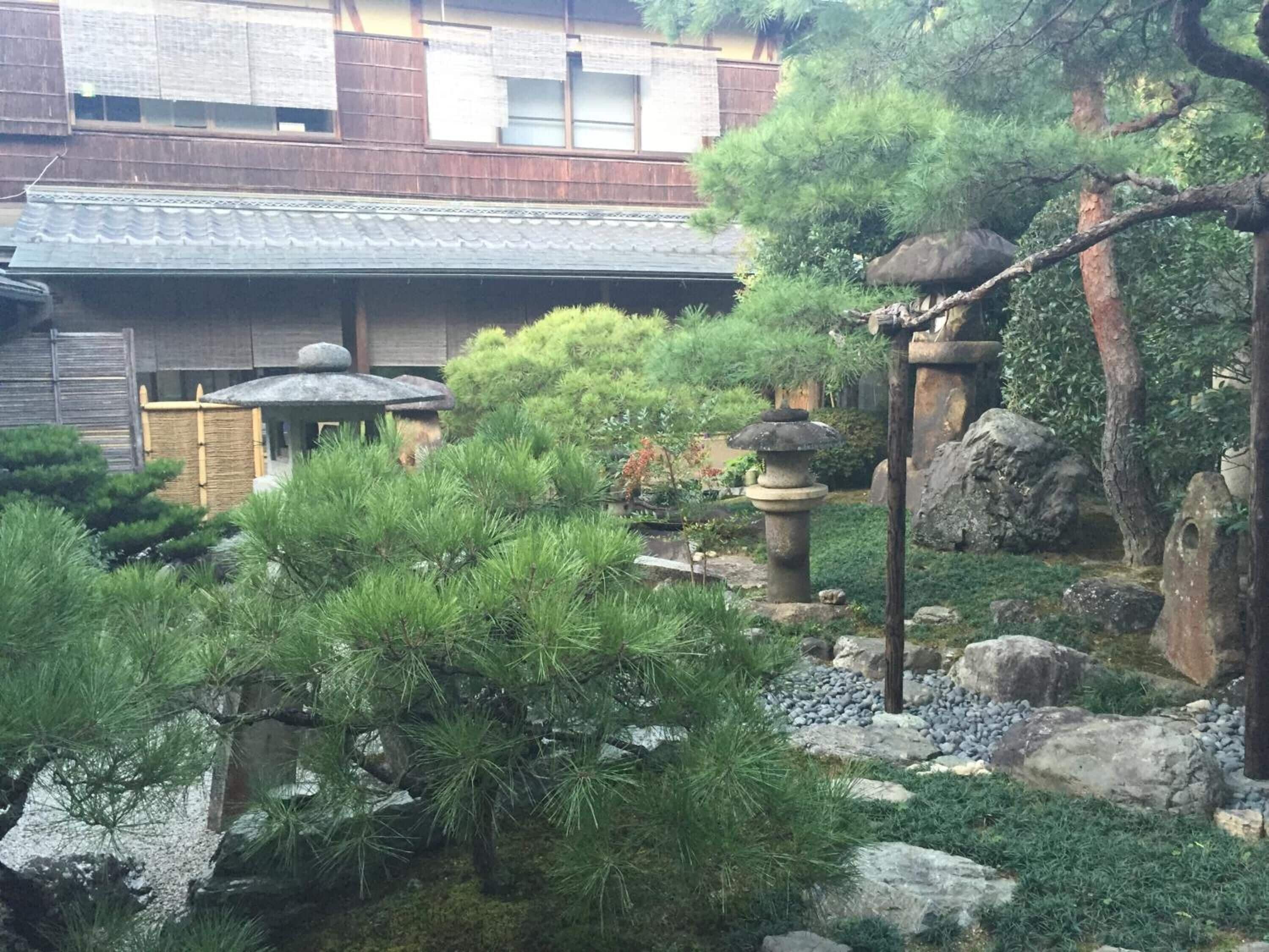Un jardin japonais traditionnel, agrémenté de lanternes en pierre, de pins et d’un bâtiment en bois surmonté d’un toit en tuiles.
