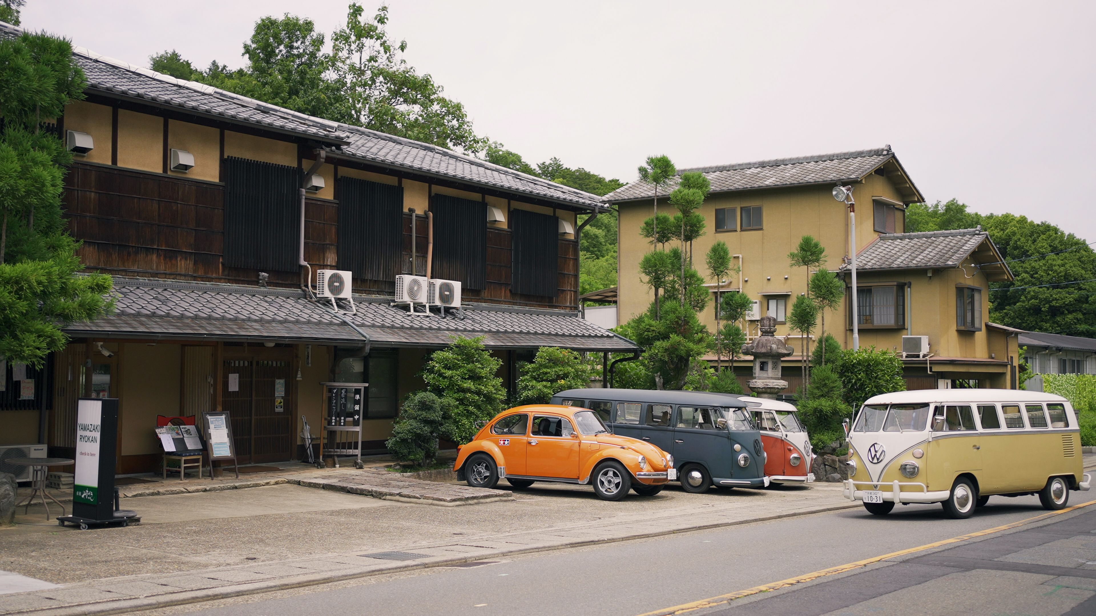 Edificio japonés tradicional con fachada de madera y tejado de baldosas, que cuenta con unidades de aire acondicionado y un pequeño espacio de estar al aire libre.