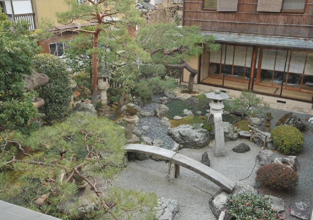 A traditional Japanese garden with a stone bridge, rocks, and a small water feature.